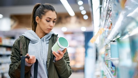 Een vrouw leest het etiket van een yoghurt op de zuivelafdeling van de supermarkt
